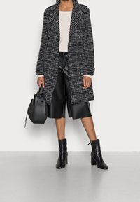 Cappotto in tweed bianco e nero con design doppiopetto, abbinato a pantaloncini in pelle nera e stivali neri con tacco fino al ginocchio. Completato da una borsa.