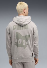 Lys grå hættetrøje med en blød tekstur, der har et grønt grafisk tryk af et katteansigt og "PUMA" tekst på ryggen. Ribbet manchetter og kant.