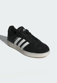 Czarne sneakersy z trzema białymi paskami, skórzany górny materiał o fakturze, otwory wentylacyjne na palcach oraz gumowa podeszwa z lekko podniesionym brzegiem.