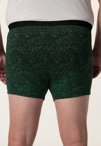 Boxer neri con un motivo floreale verde, dotati di una morbida cintura elastica e lunghezza fino a metà coscia. Tessuto dalla consistenza liscia.