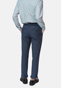 Granatowe spodnie wykonane z fakturowanej tkaniny, charakteryzujące się dopasowanym krojem, dwoma tylnymi kieszeniami z zapięciami na guziki oraz podwiniętymi nogawkami.