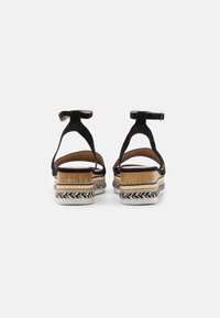 Svarta mockasandaler med ankelremmar, vävd espadrilleplattform, ljusbruna och vita accenter samt platta, texturerade sulor.