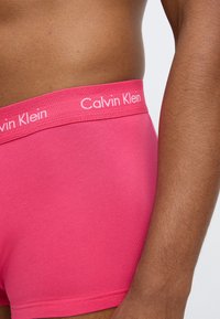 Bóxers de algodón rosa con una cintura suave que presenta la marca "Calvin Klein" en letras blancas. Textura lisa, forma ajustada y diseño minimalista.