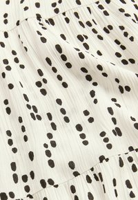 Tissu blanc avec des taches abstraites noires, présentant une apparence texturée et froissée avec des sections froncées pour un design fluide.