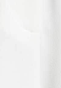 Tessuto bianco con una superficie liscia e strutturata. Presenta sottili variazioni di tonalità e lucentezza, evidenziando la sua qualità leggera e ariosa.