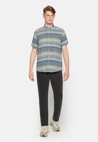 Camisa de botones de manga corta con rayas azules y beige, combinada con pantalones negros y zapatillas ligeras, con cuello y tejido texturizado.