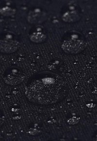 Gocce d'acqua che si accumulano su una superficie di tessuto scuro e strutturato, mostrando effetti di resistenza all'acqua e tensione superficiale.