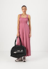 Schwarze Sporttasche mit weißen Akzenten und 'adidas'-Logo, neben einem pinken Jumpsuit mit gerafftem Oberteil und weiten Beinhosen.