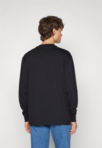 T-shirt nera a maniche lunghe con scollatura rotonda, texture liscia, vestibilità rilassata e design semplice, abbinata a jeans in denim blu.