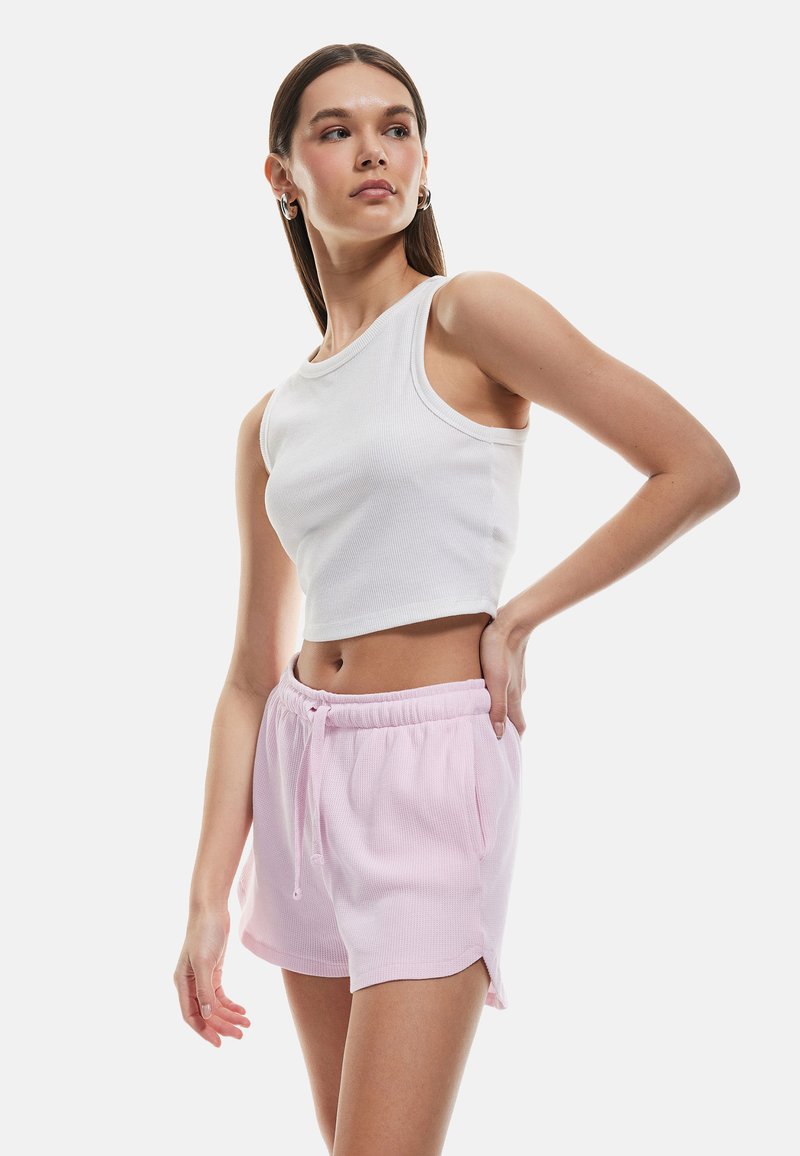 Top court côtelé blanc à col rond, associé à un short texturé rose clair avec une taille élastique et des fentes sur les côtés.