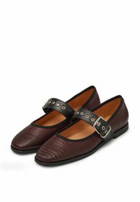 Zapatos planos burdeos con acabado texturizado, correa negra con herrajes plateados y punta redondeada. Forro interior suave.