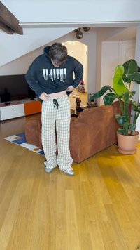 Calças de pijama em padrão xadrez cinza e branco, com cordão, combinadas com uma sweat-shirt preta com texto branco. Textura suave, ajuste largo.