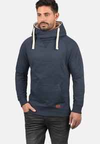 Felpa blu navy con collo alto a funnel, lacci beige, tasca a marsupio, polsini a coste e una patch in pelle sul lato inferiore.