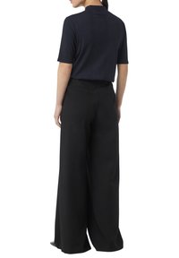 Granatowa, prążkowana bluzka z krótkim rękawem o wysokim dekolcie, w zestawie z czarnymi spodniami o szerokich nogawkach, charakteryzującymi się gładką teksturą i dyskretnymi tylnymi kieszeniami.