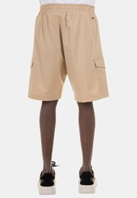 Bermuda beige con vita elastica, tasche laterali e taglio dritto. Il tessuto appare liscio con una texture leggera.