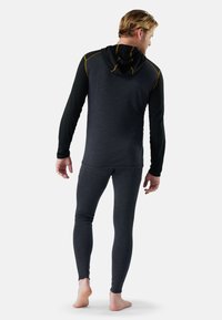 Black and gray thermal top with a hood, featuring long sleeves and yellow stitching, paired with form-fitting gray thermal leggings.