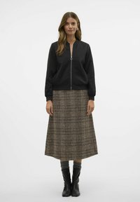 Crna bomber jakna s zatvaračem sprijeda, nošena preko smeđe karirane suknje do koljena. Model nosi čizme do koljena crne boje.