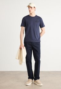 Marine bomulls T-skjorte med korte ermer, ensfarget design og logodetalj. Kombinert med mørke bukser og beige joggesko, holder en kremfarget genser.