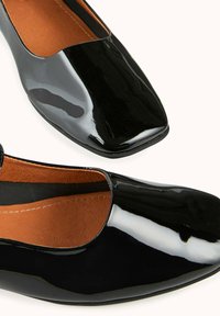 Ballerines en cuir verni noir à bout carré, dotées d'une surface lisse et brillante avec une doublure intérieure marron.