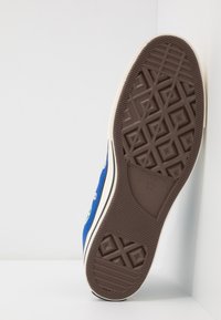 Blue canvas sneaker with white rubber trim and brown patterned sole. Features eyelets and a logo on the side, designed for casual wear.