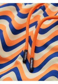 Deux cordons orange avec extrémités noires étiquetés "OMBRE" sur un tissu à rayures ondulées orange, bleues et blanc cassé.