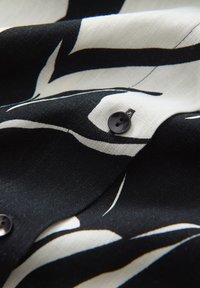 Tessuto a motivi bianco e nero con texture liscia, caratterizzato da un bottone nero e linee definite. Vista ravvicinata che si concentra sugli elementi di design.