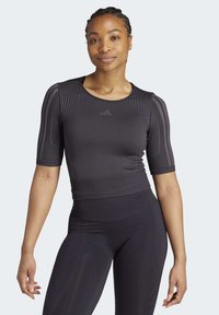 Tricou athletic cu mânecă scurtă, de culoare neagră, având o textură ribbed și modele subtile pe umeri. Fabricat dintr-un material respirabil și elastic.