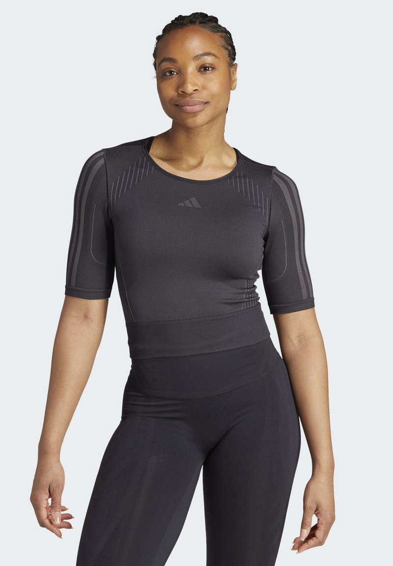 Tricou athletic cu mânecă scurtă, de culoare neagră, având o textură ribbed și modele subtile pe umeri. Fabricat dintr-un material respirabil și elastic.