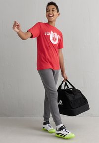 Rode t-shirt met "Zwitserland" in het wit gedrukt, gecombineerd met grijze joggingbroek, zwarte sporttas en witte/zwart/groene sportschoenen.