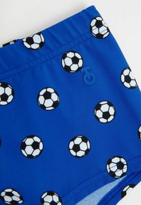 Shorts de bain bleus ornés d'un imprimé de ballons de soccer en noir et blanc, avec un accent logo bleu et une taille élastique.