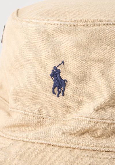 Μπεζ υφασμάτινο καπέλο τύπου κουβά με σκούρο μπλε κεντημένο λογότυπο με παίκτη πόλο πάνω σε άλογο που κρατάει υψωμένο το ρόπαλο.