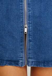 Džínová sukně s centrálním stříbrným zipem s taháčkem, modrou látkou a rovnými lemy. Texturovaný povrch s jemným vyblednutím.