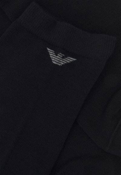 Sorte bomullssokker med ribbet tekstur. Har en grå logo brodert nær skaftet. Nærbilde som fremhever stoffdetaljene.