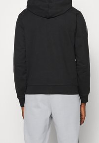 Svart huva sweatshirt med en slät textur, ribbade ärmar och nederkant, bärs med ljusgrå joggers. Enkelt design, inga synliga logotyper eller detaljer.