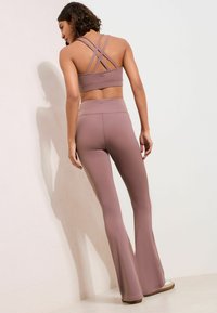 Set sportiv lila deschis, format dintr-un sutien sport cu spate cu barete și colanți evazați, realizat dintr-un material elastic cu textură netedă.