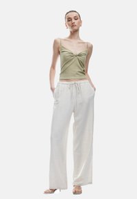 Top ajustado en verde oliva con un detalle en nudo en la parte frontal, combinado con pantalones anchos de pierna suelta en un tono beige claro, con cintura elástica.