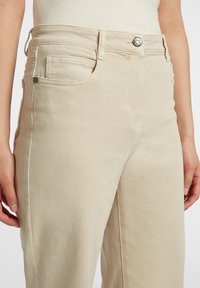 Pantaloni in cotone beige con taglio dritto, due tasche frontali, chiusura con bottone metallico e dettagli di cucitura a vista.