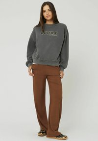 Sweatshirt gris avec le texte "OUTSIDE", associé à un pantalon large marron. L'ensemble présente une coupe décontractée et une texture douce. Chaussures noires et beiges.