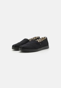 Black slip-on shoes with a textured fabric upper, lightweight and flexible sole, zigzag patterned lining, and minimalistic design.