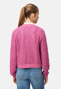 Pull rose texturé à manches longues, ourlet et poignets côtelés, coupe décontractée. Porté avec un jean bleu, vu de dos.