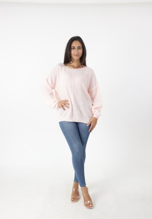 Lichtroze gebreide trui met een bootnek en verlaagde schouders; gecombineerd met denim jeans en doorzichtige hakken.