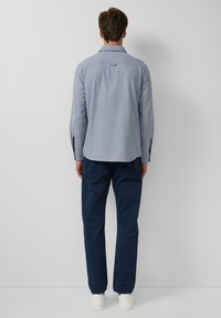 Camicia a maniche lunghe blu chiaro con colletto button-down, tessuto testurizzato e gancetto sul retro, abbinata a pantaloni blu navy e sneakers bianche.