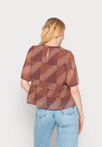 Blusa transparente com um padrão floral geométrico em castanho, laranja e azul-marinho, com mangas curtas bufantes e um detalhe nas costas em forma de gota.