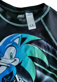 Maglietta nera a maniche corte con graphic blu di Sonic the Hedgehog. Presenta cuciture turchesi e un'etichetta di cura attaccata con i dettagli della taglia.