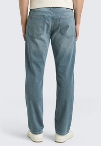 Jasnoniebieskie dżinsy z denimu o prostym kroju nogawek, z dwoma tylnymi kieszeniami i gładką fakturą. Noszone z białymi trampkami.