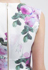 Abito floreale bianco caratterizzato da un tessuto strutturato con un motivo a diamante. Accentuato da fiori viola e verdi, include una zip dorata sul retro.