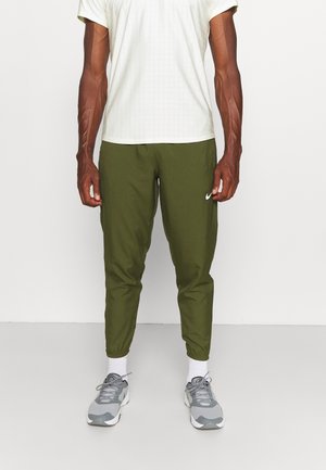 Sportovní outfit zahrnující světle šedý krátký rukáv s mřížkovým vzorem a olivově zelené zúžené kalhoty. Boty jsou šedé a bílé se šňůrkami.