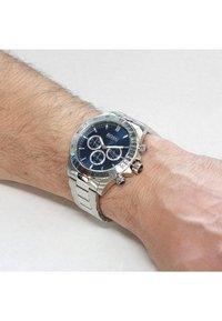Silver stainless steel watch with a dark blue dial, three sub-dials, and silver markings. The band features a polished link design.