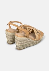 Sandali con zeppa in pelle color cuoio, tacco in paglia intrecciata e dettagli argentati. Cinghie alla caviglia regolabili per una vestibilità sicura.