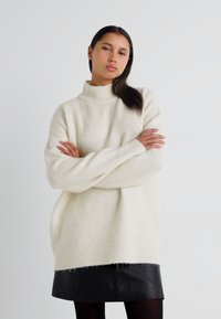 Krēmīga turtlenecks džemperis mīkstā adījumā, ar ribām pie piedurknēm un apakšmalas. Valkāts virs melnas ādas mini svārku ar frēzētiem maliņām.